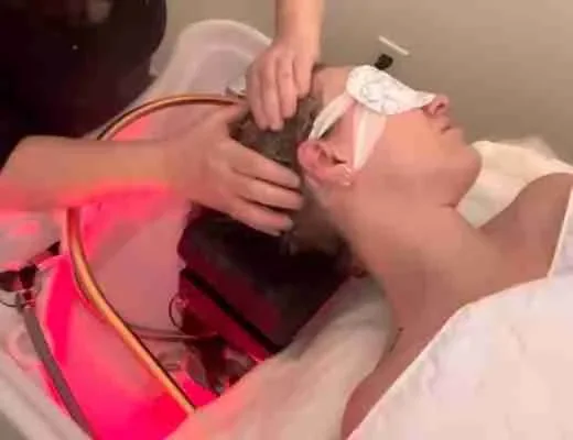 Femme allongée recevant un soin capillaire sous lumière rouge, yeux protégés.
